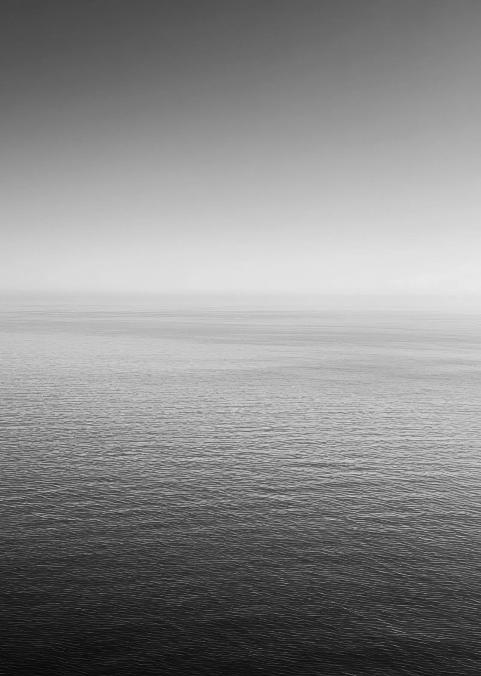 Horizonte de mar aberto sob névoa, com a água escurecendo em primeiro plano